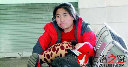 候車廳里，一位母親抱著睡著的孩子發(fā)呆